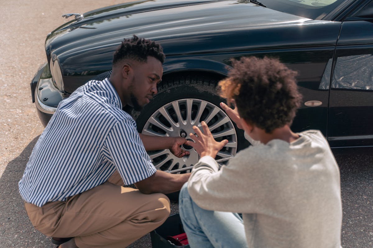 Father mentoring teenage son on how to change car tire outdoors